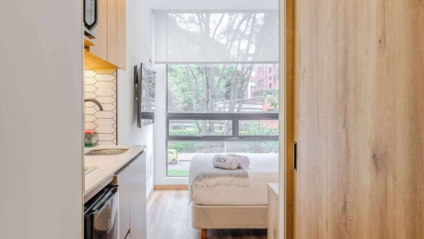 Une cuisine moderne avec des meubles en bois, un four encastré et une fenêtre donnant sur un balcon.