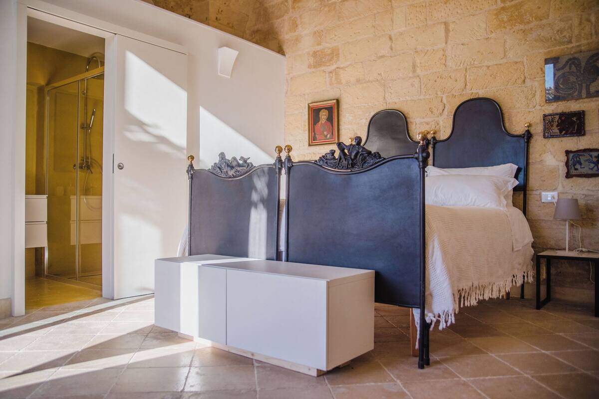 A bedroom with a bed, a bedside table, a wardrobe, and a shower area.