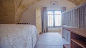 Une chambre à coucher avec un grand lit, un banc en bois et une fenêtre avec des rideaux.