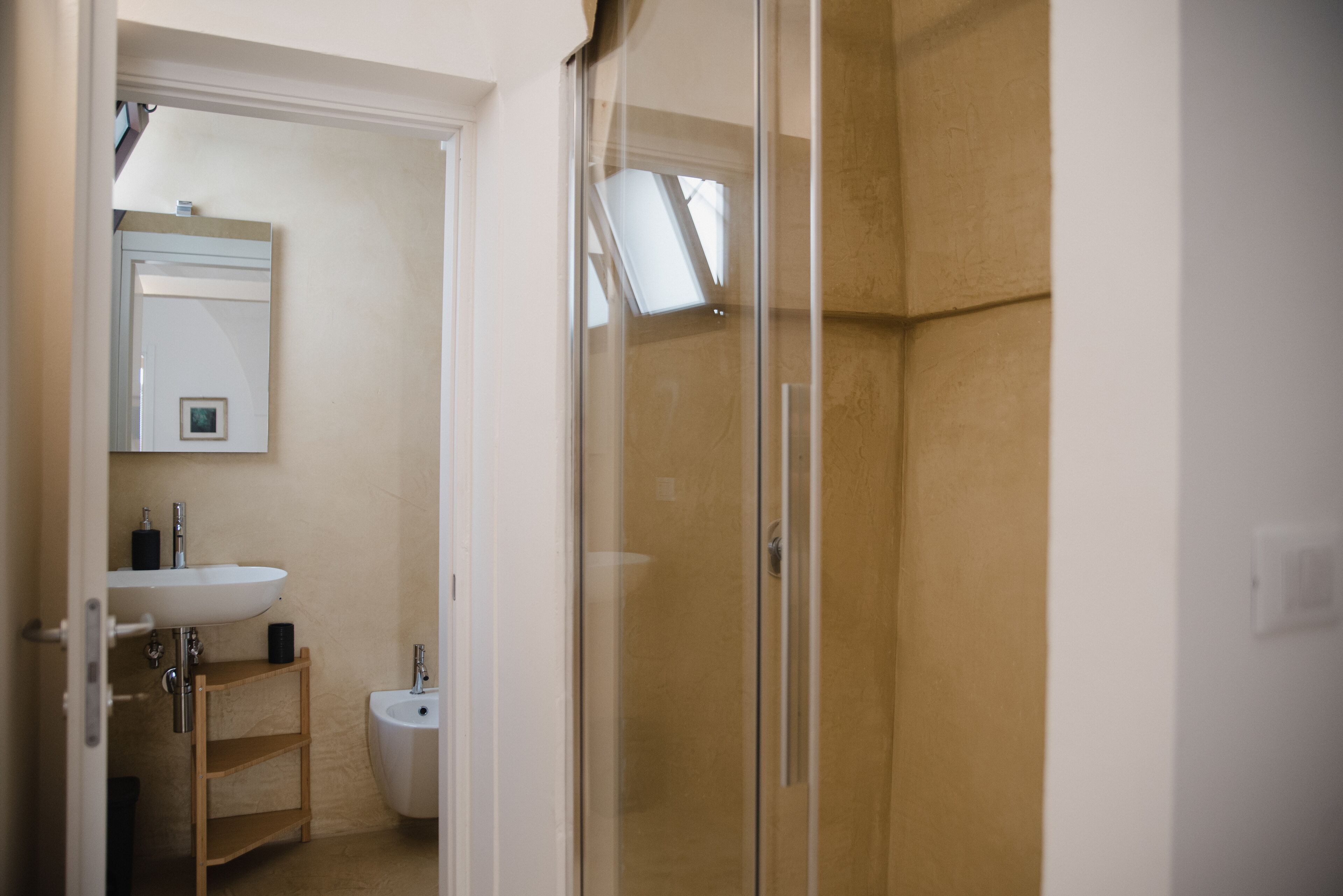 A bathroom with a white sink, a mirror, a bidet, and a glass shower enclosure.