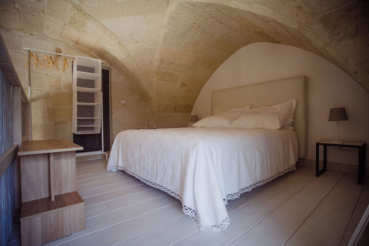 A bedroom with a large bed, a wooden nightstand, a white dresser, and a built-in shelving unit.