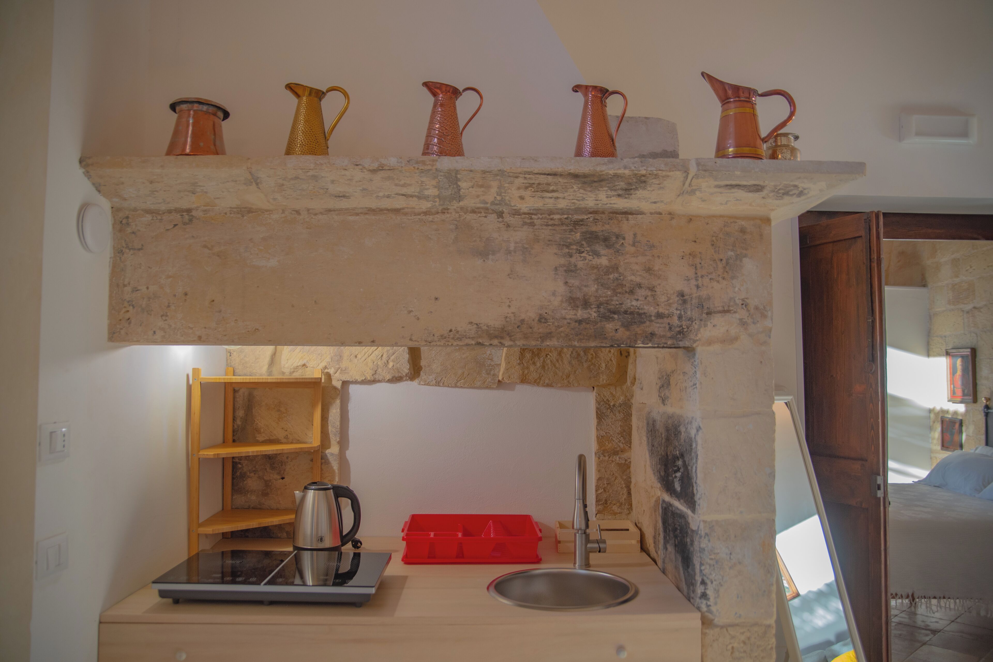 Una cocina con encimera de piedra, un lavamanos y una estantería con cinco jarras.