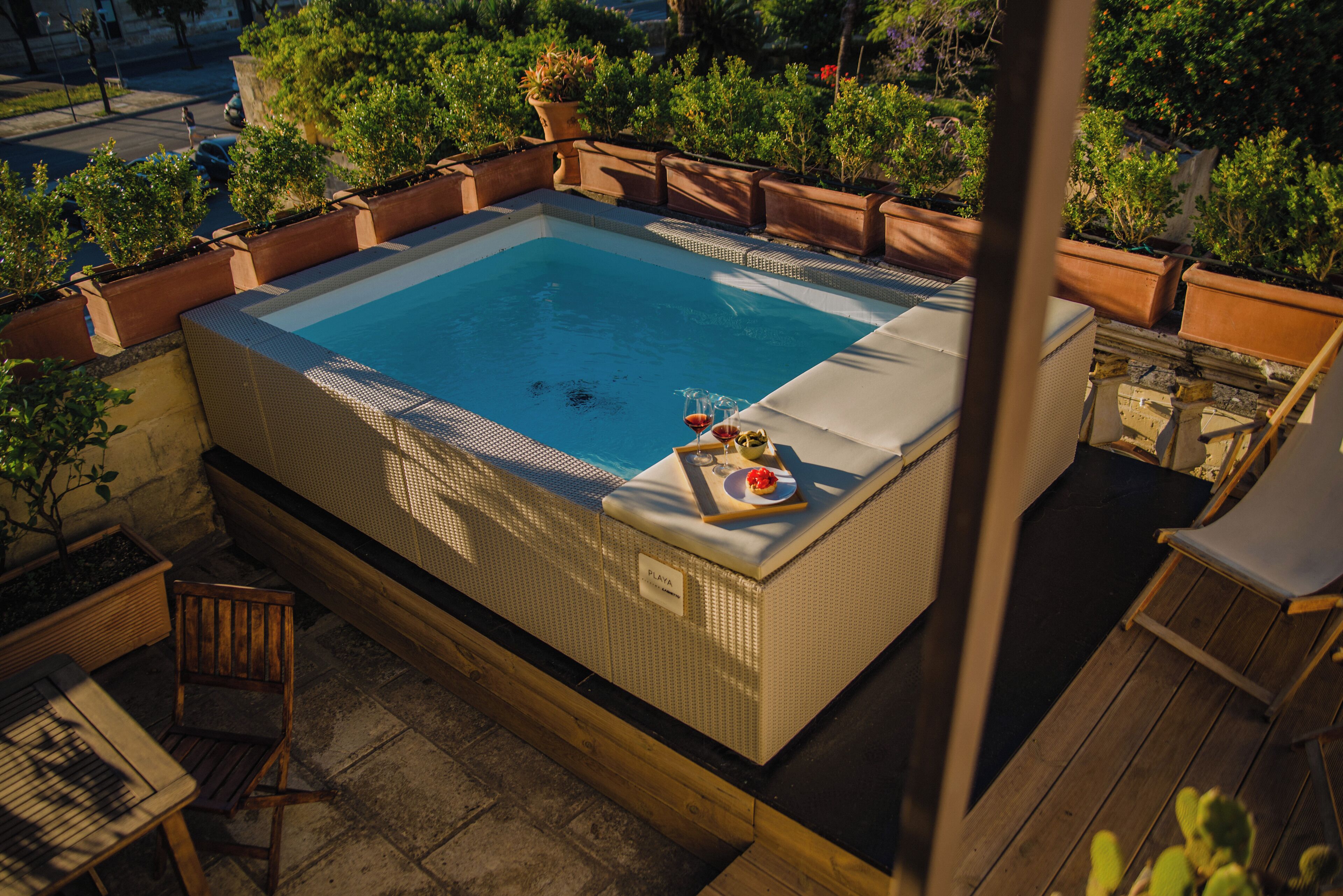 Een hottub met zwembad, omringd door potplanten en houten meubels.