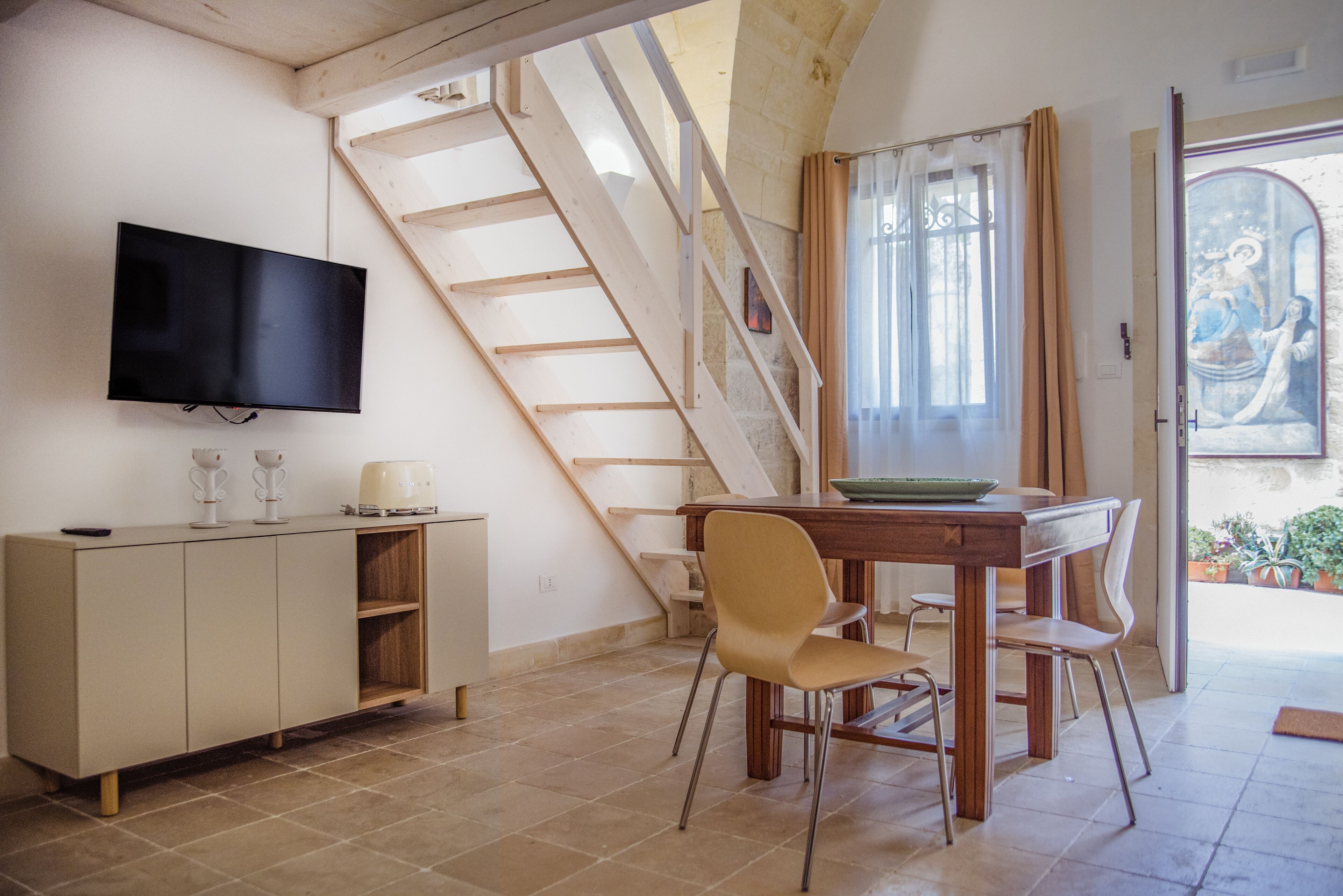 Ein Essbereich mit Holztisch und Stühlen, einem an der Wand befestigten Fernseher und einer Treppe zu einer anderen Ebene.