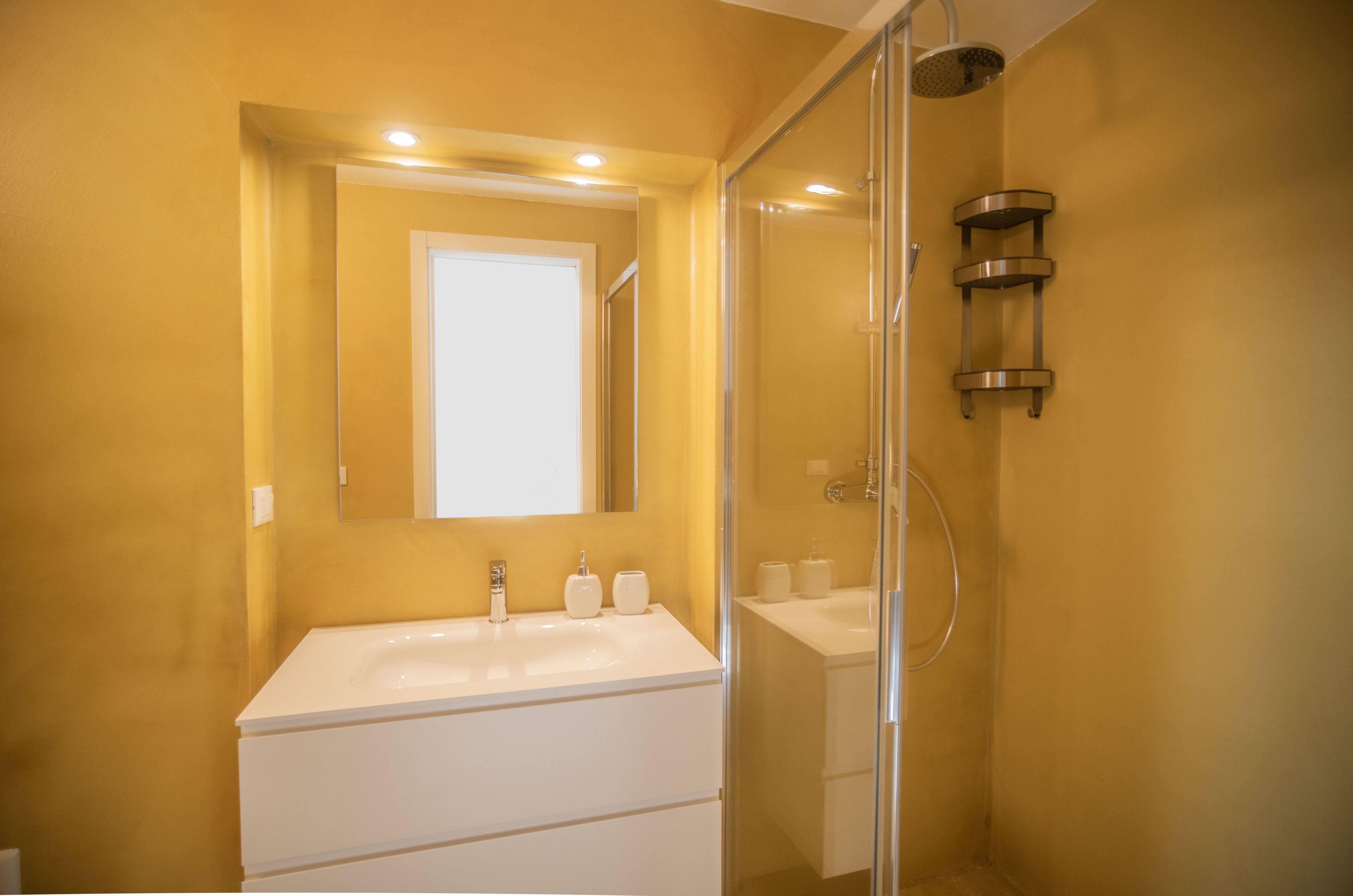 Ein Badezimmer mit einem weißen Waschbecken, einem Spiegel und einer Duschkabine aus Glas.