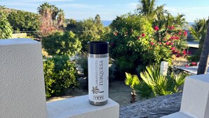 A YETI branded water bottle on a white surface with a view of a garden and palm trees in the background.