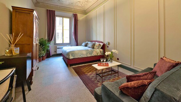 Un dormitorio con cama, escritorio, silla, sofá y ventana con cortinas.