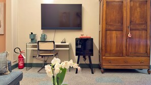 A room with a flat-screen TV mounted on the wall, a wooden cabinet, a desk with a chair, and a vase with white flowers. - Cinisca Suite Blue in Bologna (Bologna)