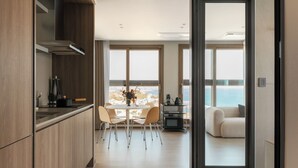 A modern kitchen with wooden cabinets, a dining area with a table and chairs, and a view of the sea through large windows. - Plott The One Sokcho Xiella The Beach (Sokcho)