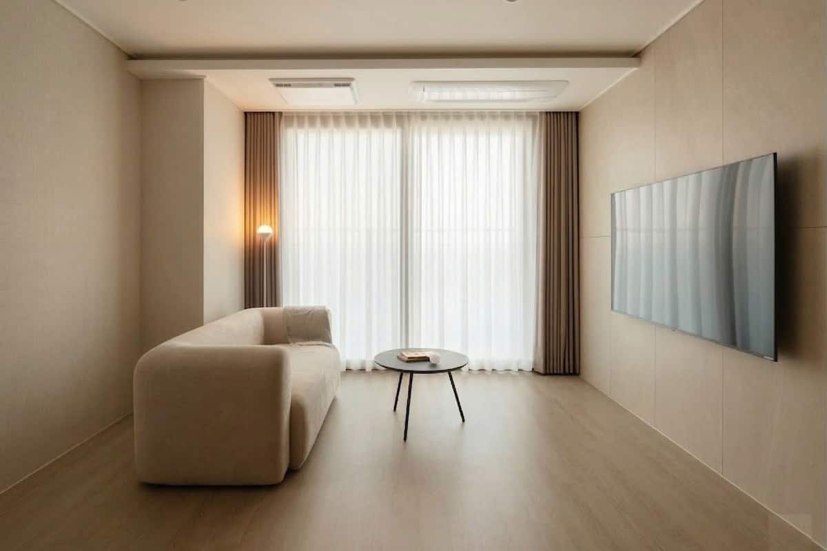 Une chambre d’hôtel moderne, dotée d’un canapé, d’une petite table ronde, d’un téléviseur à écran plat fixé au mur et d’une grande fenêtre avec des rideaux.