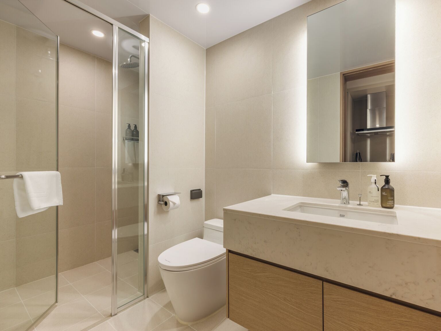 Un baño moderno con cabina de ducha de vidrio, inodoro y tocador con lavamanos y espejo.