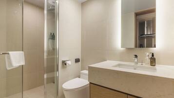 Un baño moderno con cabina de ducha de vidrio, inodoro y tocador con lavamanos y espejo.