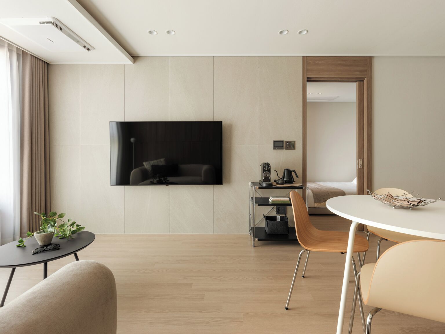 Une chambre d’hôtel moderne équipée d’un téléviseur à écran plat fixé au mur, d’un bureau avec une chaise, d’une table de salle à manger ronde et d’un lit avec une tête de lit en bois.