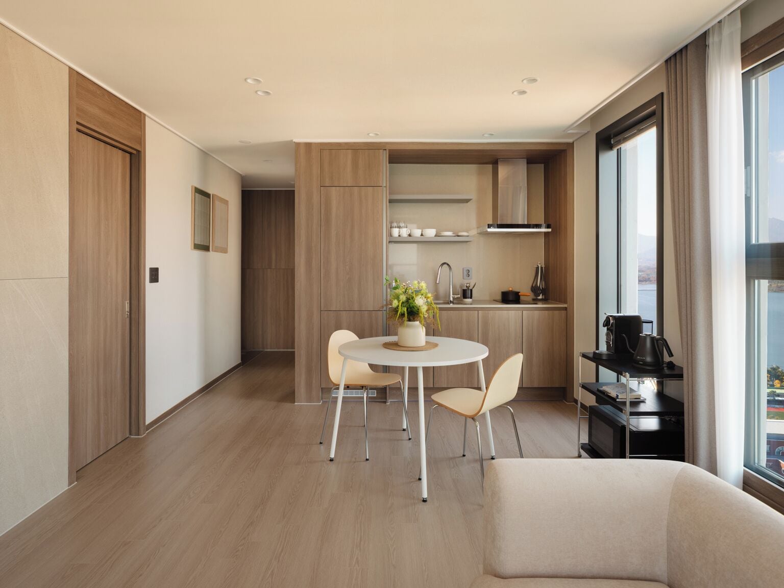 A modern, well-lit room with a dining area, a sofa, and a kitchen area with a view.