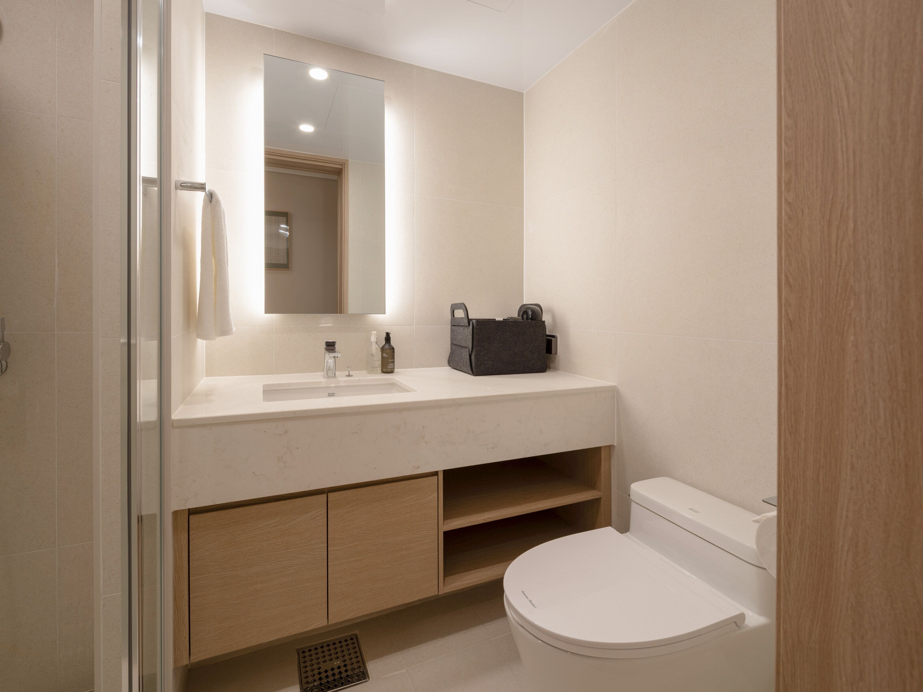 A modern bathroom with a white sink, mirror, and toilet. There is a wooden cabinet below the sink and a shower area to the left.