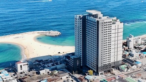 A high-rise hotel adjacent to a beach with clear blue waters and a rocky breakwater. - Plott The One Sokcho Xiella The Beach (Sokcho)