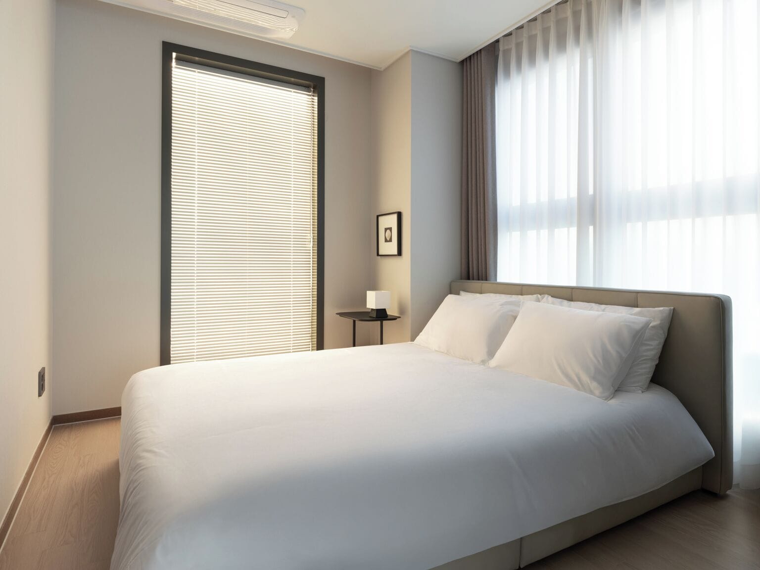 Una habitación de hotel moderna con una cama grande, una mesita de noche con lámpara y una ventana con persianas.