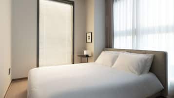 Una habitación de hotel moderna con una cama grande, una mesita de noche con lámpara y una ventana con persianas.