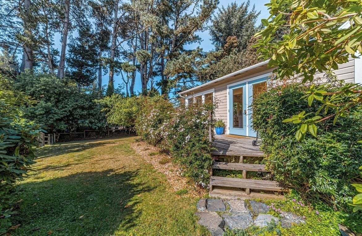 A house with a wooden deck, surrounded by lush greenery and tall trees.