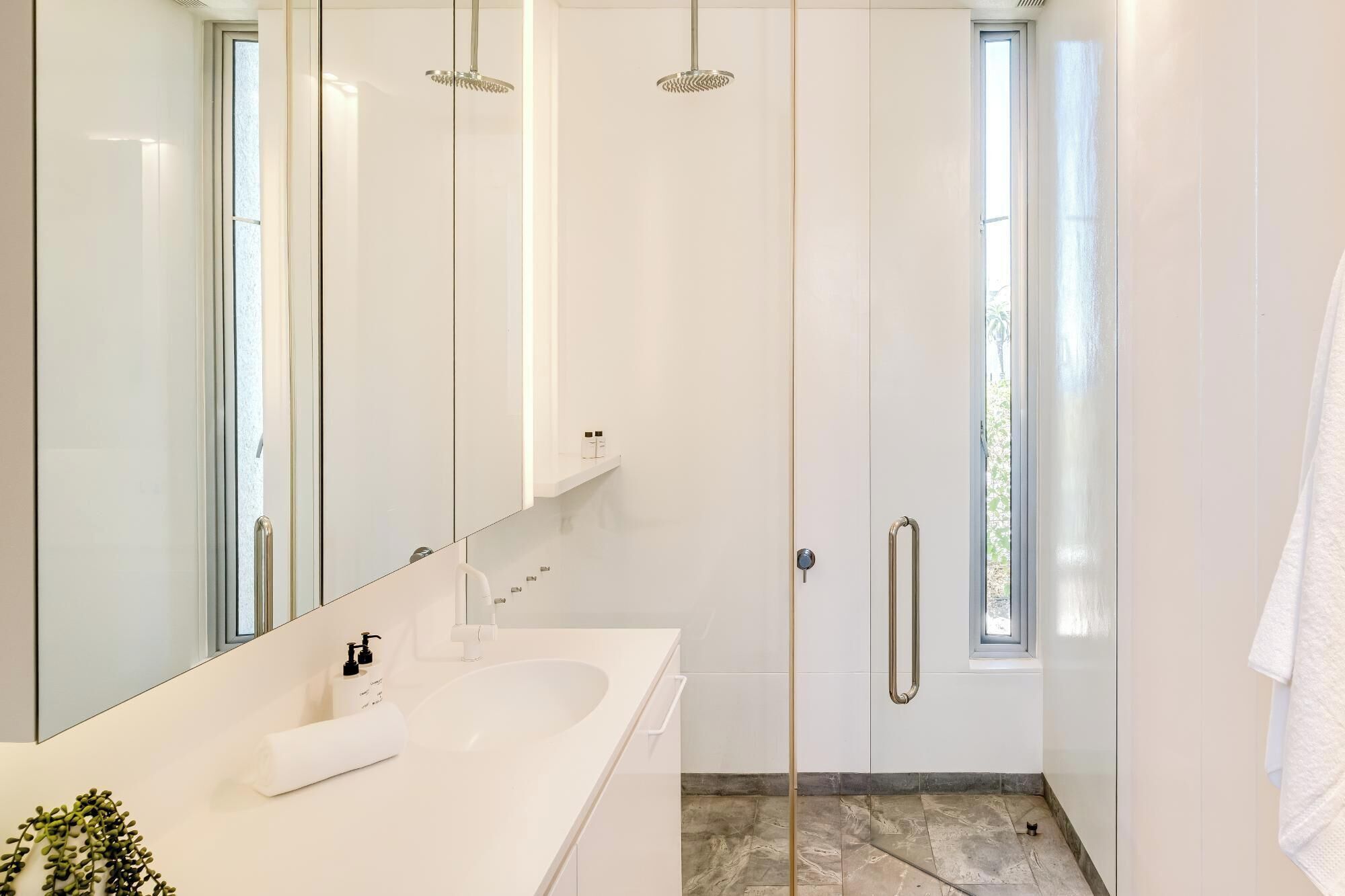 A modern bathroom with a large mirror, a white sink, and a shower with a glass door.