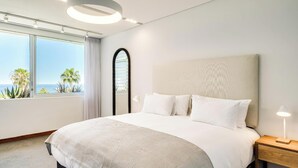 Una habitación de hotel moderna con una cama grande, vista al océano y un diseño minimalista.
