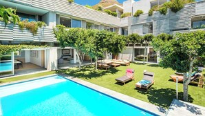 Un hotel moderno con piscina, mobiliario exterior y abundante vegetación.