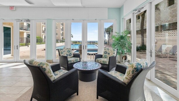 A sunlit indoor seating area with wicker furniture and a central glass-top table, overlooking a pool and outdoor seating. - 510 - Cozy 1 bedroom Fantastic View (New Smyrna Beach)