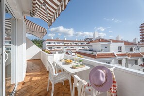 A balcony with a white table, chairs, and a hat, overlooking a residential area with red-tiled roofs. - Vacation Apartment "Golden Sun Penthouse" with Shared Pool, Private Terrace & Wi-Fi (Playa de las Américas)
