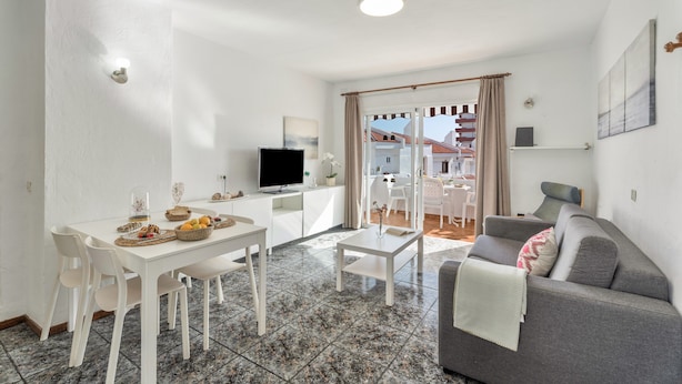 Een moderne woonkamer met een eethoek, een grijze bank, een flatscreen televisie en een balkon met uitzicht.
