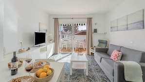 Een moderne woonkamer met een flatscreen televisie, een eettafel met een fles wijn en een bank met een kussen.
