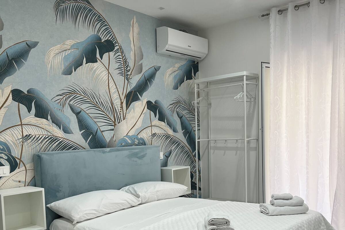 A bedroom with a bed, a shower, and a wall with a tropical leaf mural.