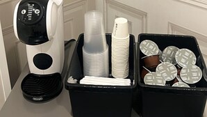 A coffee machine, stacked plastic cups, and a container with lids on a table against a door. - Casa Margherita  (Naples)