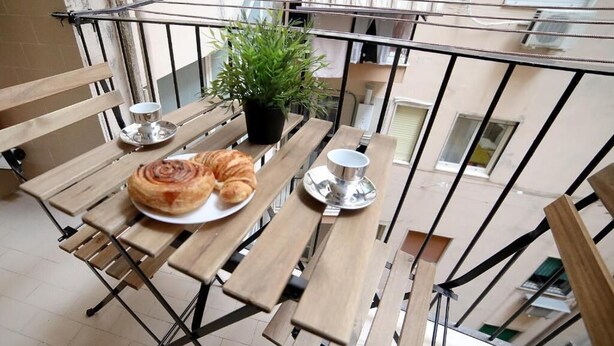 A balcony with a wooden table, a potted plant, and a croissant on a plate. - Casa Margherita  (Naples)