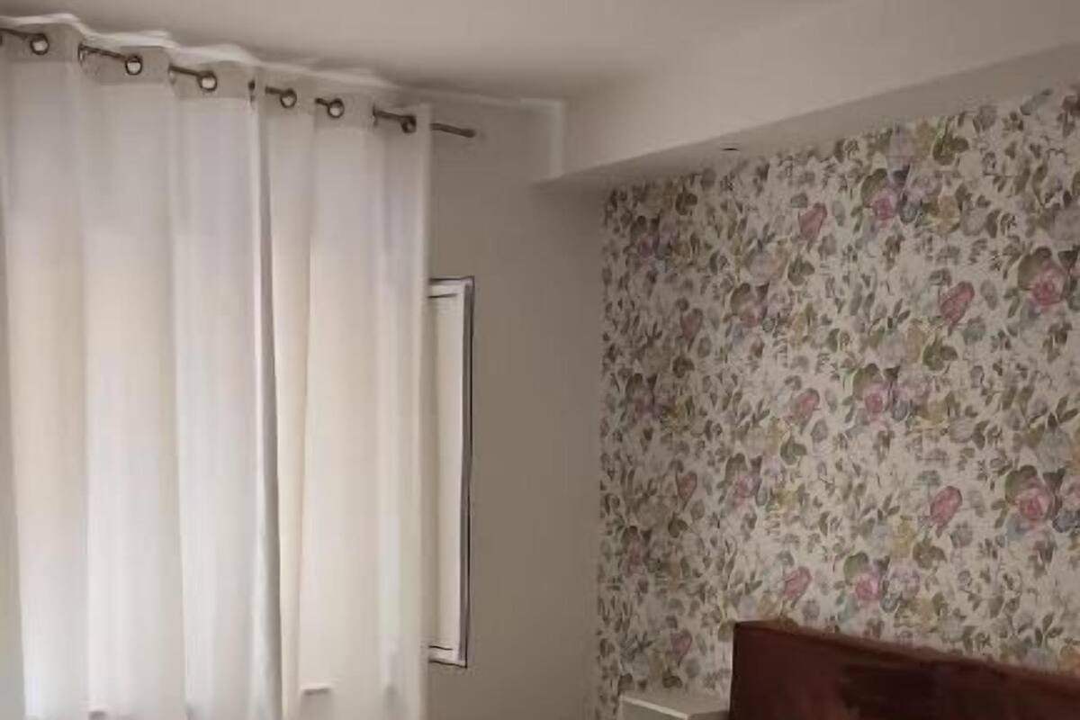 A bedroom with a bed, a nightstand, and a window with curtains.