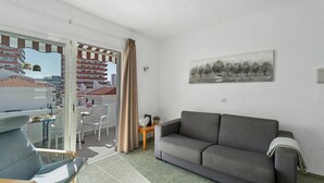 A living room with a sofa, a chair, a small table, a painting, and a view through a glass door. - Ocean Breeze Penthouse Apartment with Shared Pool, Private Terrace and Wi-Fi (Playa de las Américas)