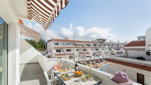 A balcony with a table, a hat, and a view of a building with multiple balconies. - Ocean Breeze Penthouse Apartment with Shared Pool, Private Terrace and Wi-Fi (Playa de las Américas)