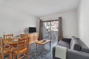 A living room with a sofa, wooden dining table, chairs, a TV, and a balcony with outdoor seating. - Blue Pool Las Floritas Apartment with Shared Pool, Private Terrace and Wi-Fi (Playa de las Américas)