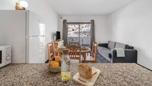 Eine kleine Küche mit Essbereich, ein graues Sofa und Blick auf ein Wohnhaus.
