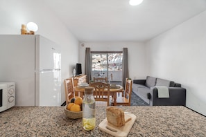 A compact kitchen with a dining area, a grey sofa, and a view of a residential building. - Blue Pool Las Floritas Apartment with Shared Pool, Private Terrace and Wi-Fi (Playa de las Américas)