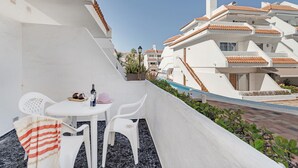 Ein Balkon mit weißen Stühlen und einem Tisch, ein kleiner Pool und Gebäude mit Terrakotta-Dächern.