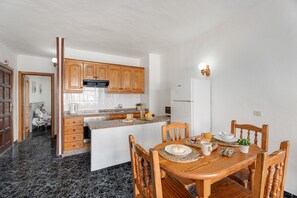 A compact kitchen with wooden cabinets, a central island, and a dining area with wooden chairs. - Blue Pool Las Floritas Apartment with Shared Pool, Private Terrace and Wi-Fi (Playa de las Américas)