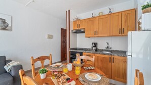 A dining area with a wooden table, chairs, and a breakfast setting including bread, fruits, and juice. - Apartment Infinity Pool Views with Shared Pool, Private Terrace and Wi-Fi (Playa de las Américas)