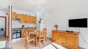 A compact kitchen with wooden cabinets, a dining table with chairs, a built-in oven, and a flat-screen TV mounted on the wall. - Apartment Infinity Pool Views with Shared Pool, Private Terrace and Wi-Fi (Playa de las Américas)