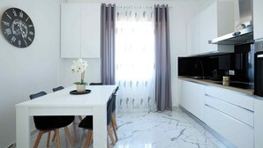 Een moderne keuken met witte kasten, een marmeren vloer, een eettafel met stoelen en een klok aan de muur.