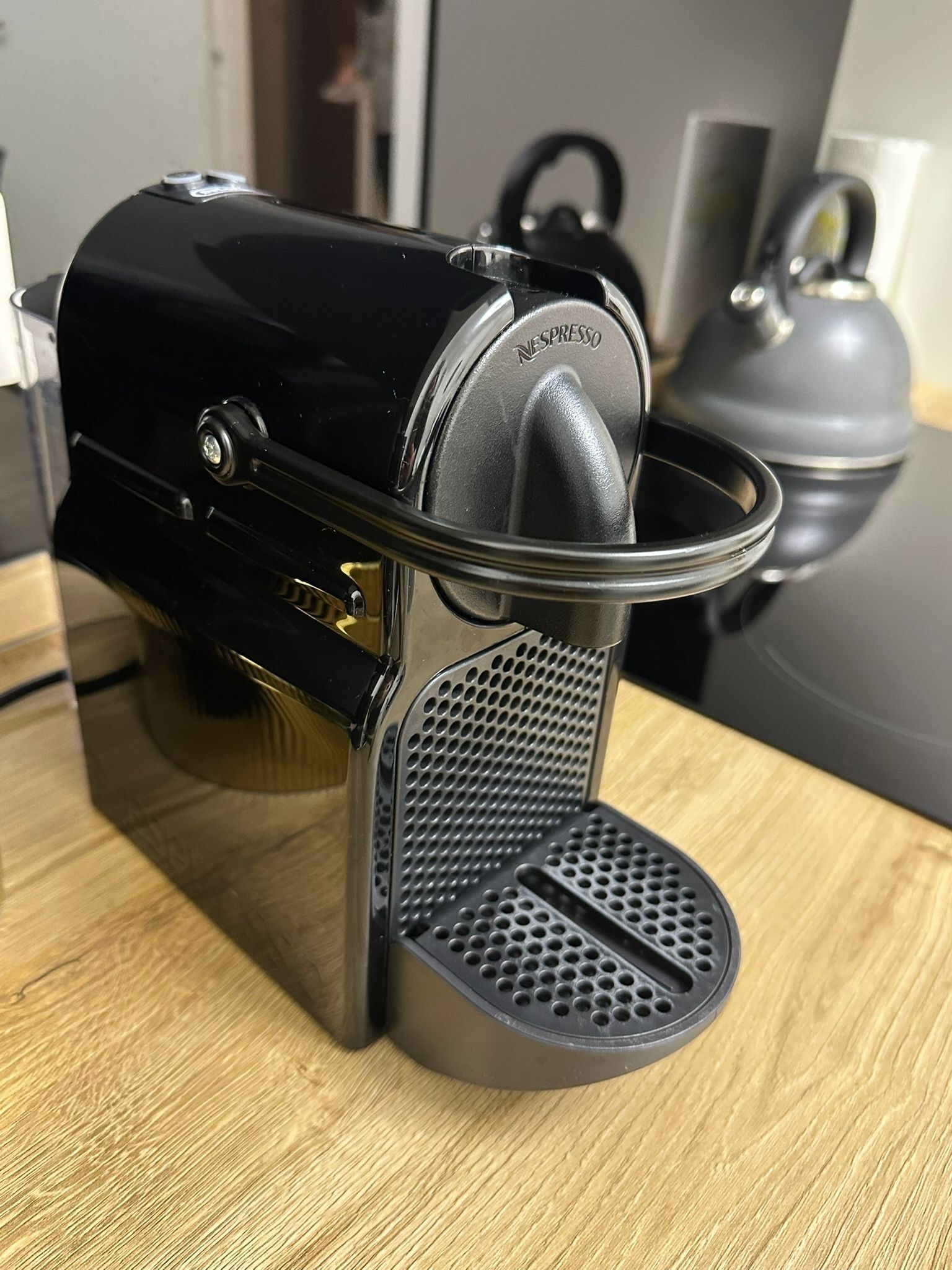 En sort espressomaskine med et metalhåndtag og en perforeret bund, placeret på en træoverflade.