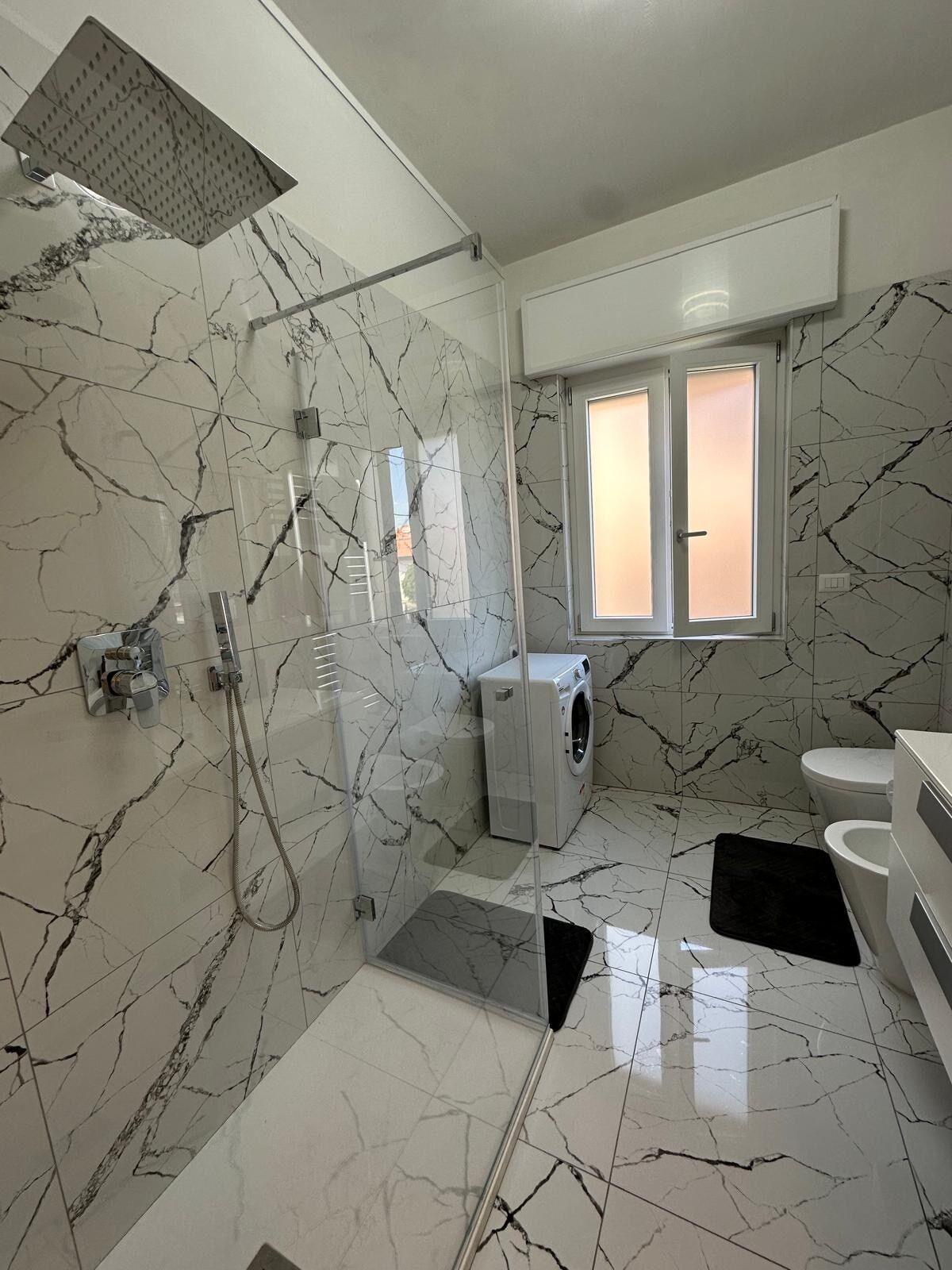A modern bathroom with a glass-enclosed shower, a built-in washing machine, and a toilet.