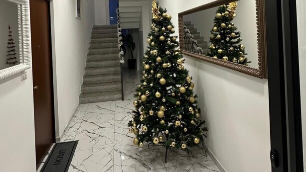 Een gang met een marmeren vloer, een kerstboom, een spiegel en een trap op de achtergrond.