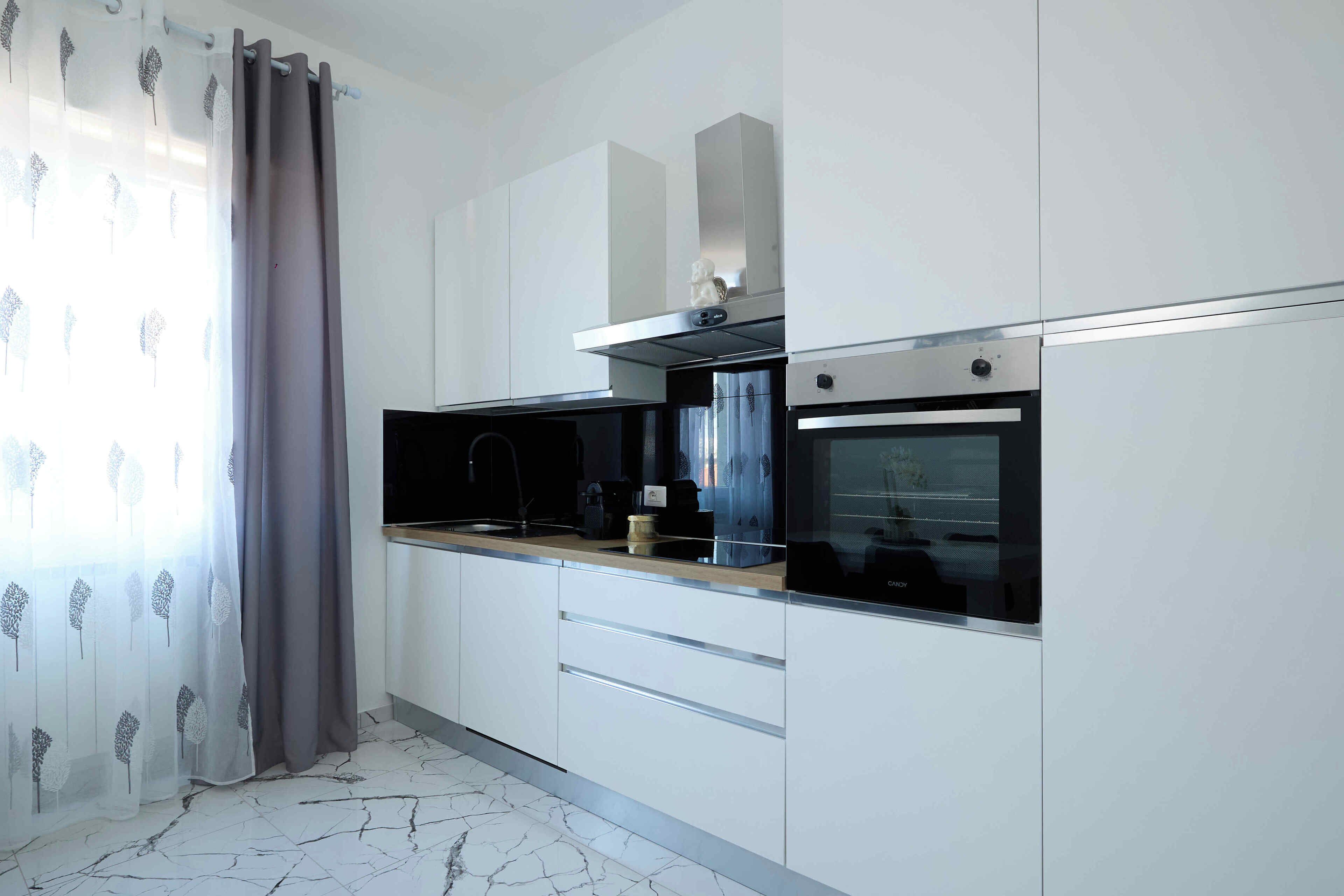 Een moderne keuken met witte kasten, een zwart aanrecht, een ingebouwde oven en een rvs afzuigkap.