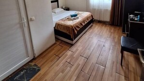 A bedroom with a bed, a desk, and a chair. There is a window with curtains, an air conditioning unit, and a door. - Üsküdar Hotel Batum (Batumi)