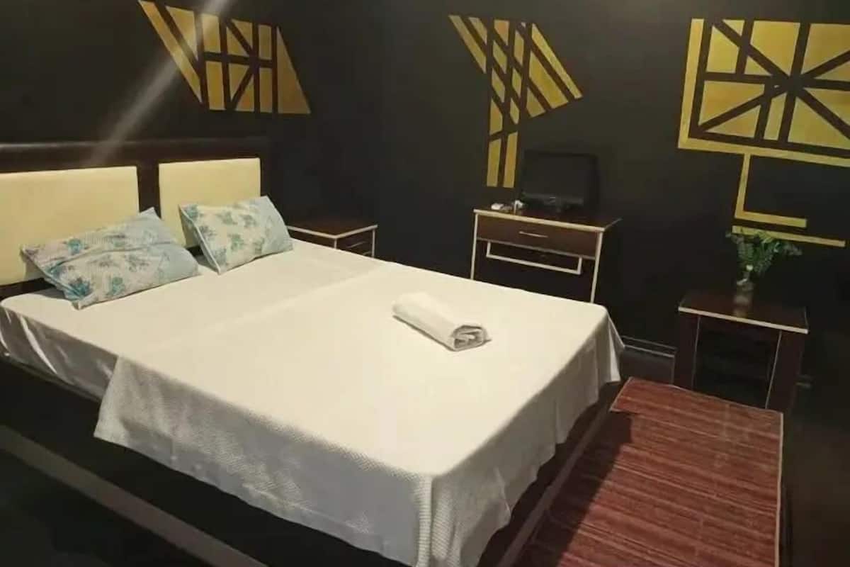 A hotel room with a bed, bedside tables, a dresser, and decorative wall art.